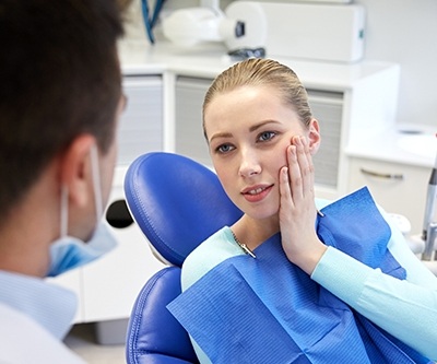 Young woman in dental chair holding the side of her face