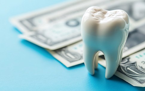 Large model tooth on light blue surface next to dollar bills