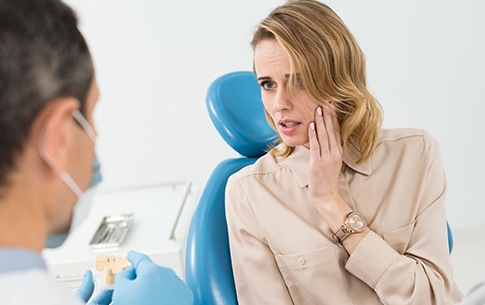 Woman in dental chair holding cheek