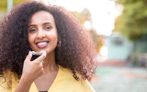 Woman smiling while holding Invisalign clear aligner