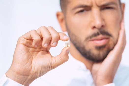 Man holding extracted tooth in one hand and pressing other to sore jaw