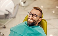Man with glasses smiling while sitting in treatment chair