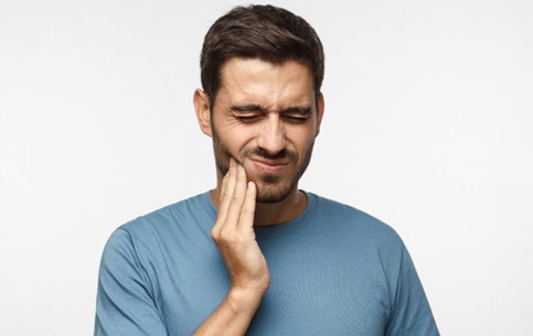 Man in blue shirt rubbing jaw in pain