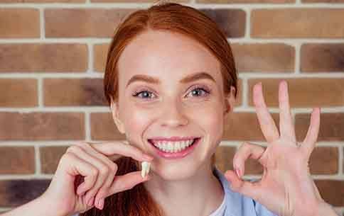 A smiling red-haired girl holding a wisdom tooth extracted from her mouth