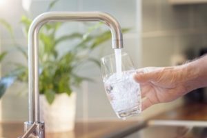 Man gathering tap water in a glass from his kitchen sink