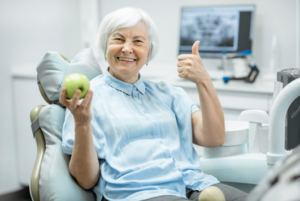 Woman in patient’s chair holding an apple and giving a thumb’s up