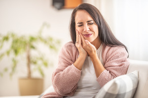 Woman in pink sweater sitting on couch with toothache
